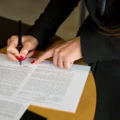 Dłoń z czerwonymi paznokciami podpisuje dokument piórem.
